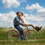 A man riding a woman on a bicycle in an open field