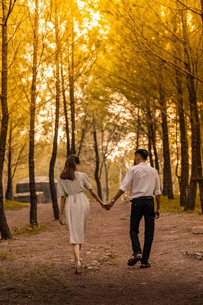 A man and a woman walking while holding hands in a forest 